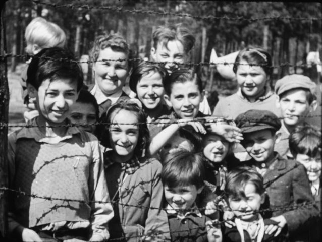 Usmívající se děti za ostnatým drátem zachycené seržantem Lewisem 19. - 20. dubna 1945. Zdroj: IWM 